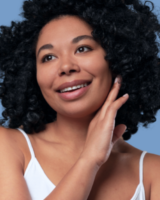 Woman with curly hair smiling, touching face, on a blue background