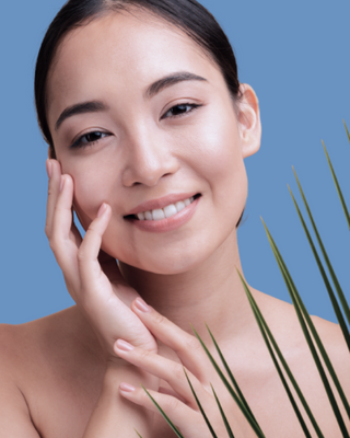 Smiling woman touching face with green leaves on the side, on a blue background.