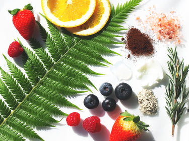 Various berries, leaves, and beauty product ingredients laid out on a white surface