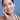 Smiling woman touching face with green leaves on the side, on a blue background.