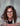 Woman with long, curly, brown hair and black glasses wearing a lab coat smiling behind beakers